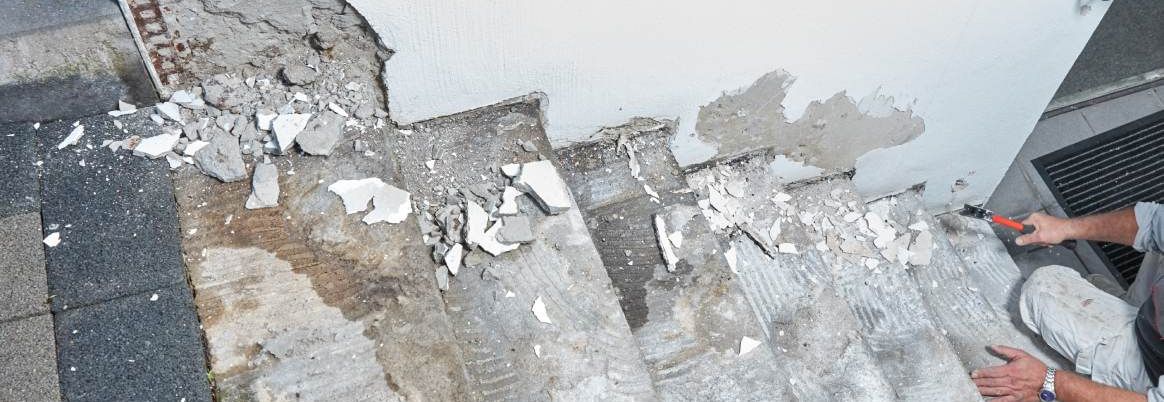 Eine Person saniert eine kaputte Betontreppe mit einem Werkzeug.